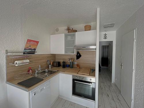 une cuisine avec des armoires blanches, un évier et une cuisinière dans l'établissement Appartement 4 personnes avec climatisation et parking aux Saintes-Maries-de-la-Mer - FR-1-475-182, à Saintes-Maries-de-la-Mer