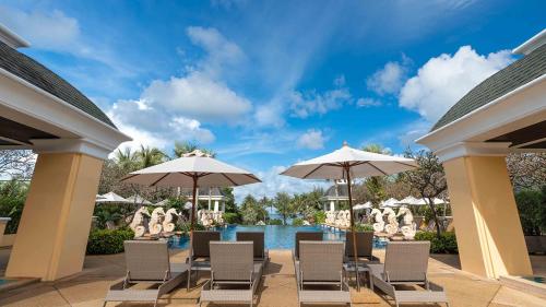 eine Terrasse mit Stühlen und Sonnenschirmen neben einem Pool in der Unterkunft Phuket Graceland Resort and Spa in Patong Beach