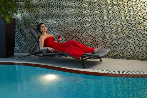 a woman in a red dress sitting in a chair next to a pool at Cristal Hotel Abu Dhabi in Abu Dhabi