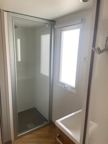 La salle de bains est pourvue d'une douche en verre et d'une fenêtre. dans l'établissement Mobil home vias La Carabasse, à Vias