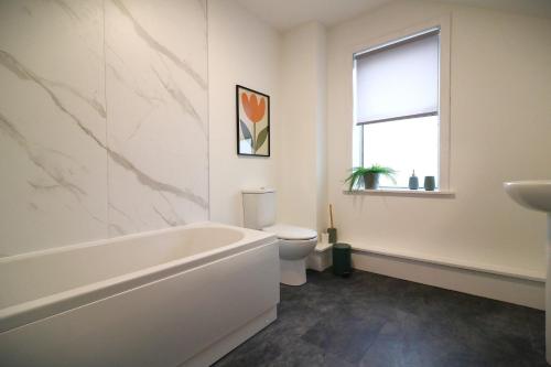 a bathroom with a tub and a toilet and a window at Signature - St James House in Abbotsinch