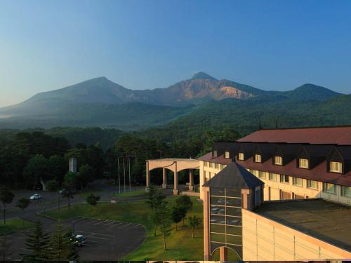 a large building with mountains in the background at Urabandai Lake Resort Goshiki no Mori in Kitashiobara