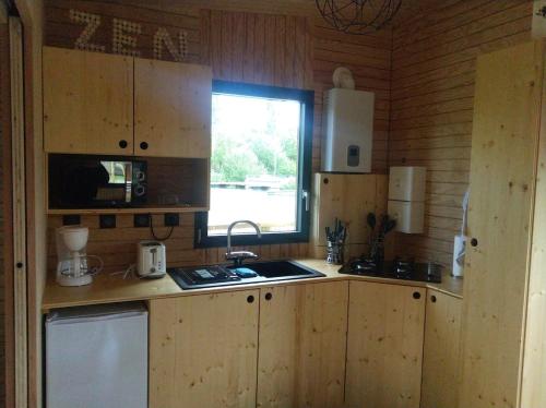 une cuisine avec des armoires en bois, un évier et une fenêtre dans l'établissement tom Sawyer cabane flottante, à Bressuire