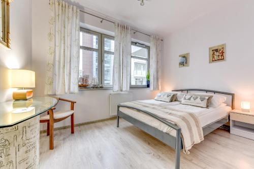 a bedroom with a bed and a desk and windows at Aqua by Grand Apartments in Gdańsk