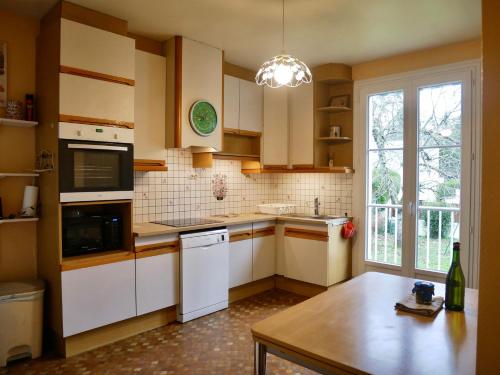 une cuisine avec des armoires blanches, une table et une fenêtre dans l'établissement La maison des retrouvailles aux portes de Tours, à Saint-Avertin