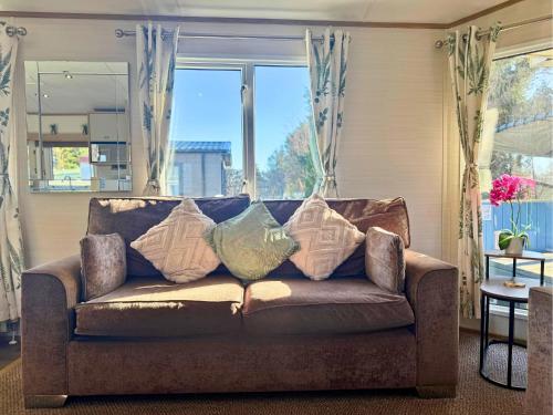 a couch with pillows on it in front of a window at Private Hot Tub & Spacious Decking Area in Northumberland, Dog-Friendly, Free Golf Access in Swarland