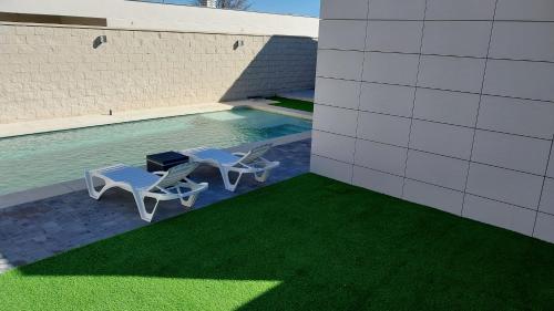 2 Stühle und ein Pool mit grünem Gras in der Unterkunft La Casita de la Piscina in Burguillos de Toledo