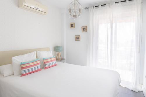 biała sypialnia z białym łóżkiem i żyrandolem w obiekcie La Marina Suite Málaga w Maladze