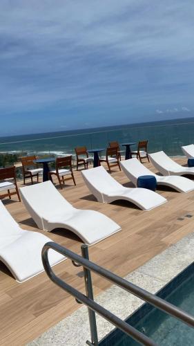 a row of white lounge chairs and tables on a deck at 805 Vista Mar Aconchegante in Salvador