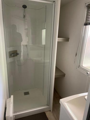 La salle de bains est pourvue d'une douche en verre et d'un lavabo. dans l'établissement Camping Rivages des Landes Mobil-home climatisé et Tv, à Aureilhan