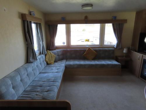 a living room with a blue couch in front of a window at 3 bedroom static caravan with sea view in Clarach Bay Holiday Village Abi horizon in Aberystwyth