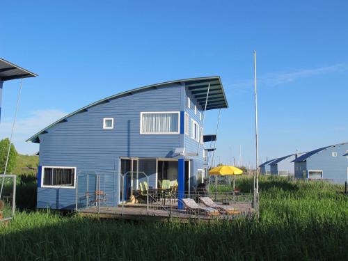 a blue house with a gambrel roof on a field at Ferienhaus SEABIRD by FeWo-PLAN OOST150 mit direktem Zugang ins LAUWERSMEER in Anjum