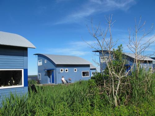 a person sitting on a bench in front of a blue building at Ferienhaus SEABIRD by FeWo-PLAN OOST150 mit direktem Zugang ins LAUWERSMEER in Anjum