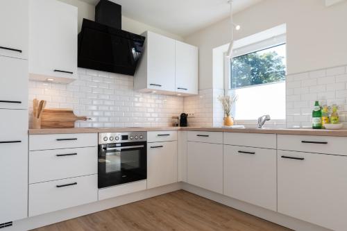 a white kitchen with white cabinets and a sink at Küstenbutze im modernen Scandi-Style mit Garten und Terrasse in Mildstedt