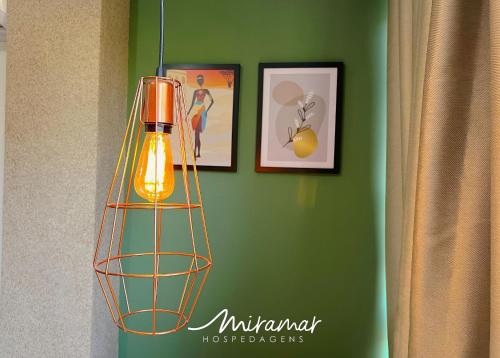 a lamp hanging on a green wall with two pictures at Vert House Jardim Oceania - Miramar Hospedagens in Tambaú