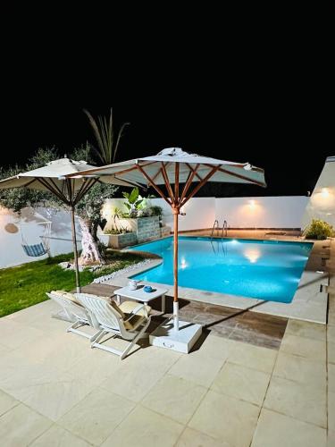 einen Pool mit 2 Sonnenschirmen, 2 Stühlen und einem Tisch in der Unterkunft Dar Mami in Al Maqārisah
