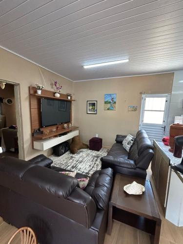 a living room with a leather couch and a flat screen tv at Rancho Lopes - Casa com piscina e churrasqueira, Iguape-SP in Iguape