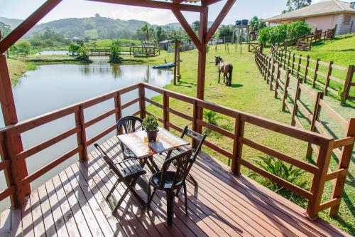 a table and chairs on a deck next to a river at Chalé Rústico com Hidromassagem e Piscina in Imaruí