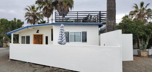 a white house with a blue roof behind a white fence at CASA COLIBRI - BEACH LIVING AT ITS BEST in Ensenada