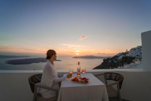 a woman sitting at a table with glasses of wine at Spitia Tzitzi in Imerovigli