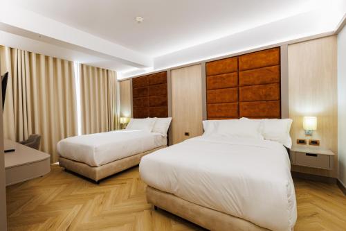 two beds in a hotel room with white sheets at Hotel Fieri in Fier