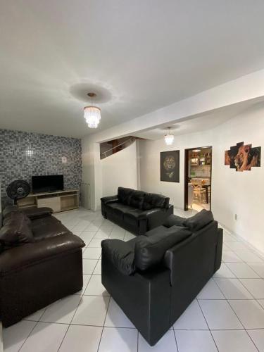 a living room with black leather couches and a tv at Casa Em Pirangi Praia - RN in Parnamirim