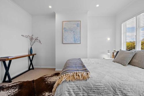 ハミルトンにあるElegant Hamilton East Home Near Gardens and Cafesの白いベッドルーム(ベッド1台、テーブル付)