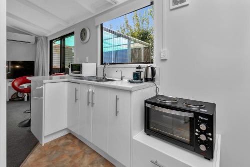 a white kitchen with a sink and a microwave at Cottage on Churchill in Whangarei