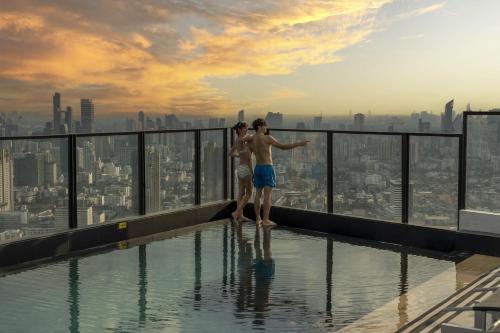 a man and a woman standing on the edge of a swimming pool at Cassia Rama 9 Bangkok, part of Banyan Group in Bangkok
