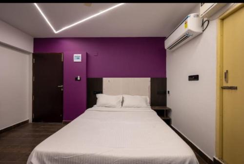 Cama grande en habitación con pared morada en The Magnum Inn, en Unamaucheri