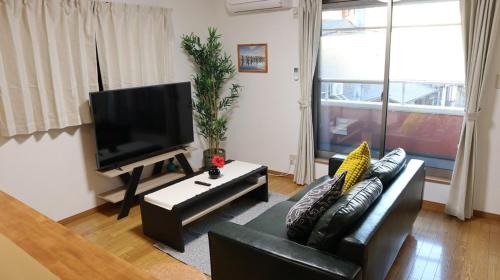 a living room with a black couch and a flat screen tv at 駅徒歩1分 観光拠点に最適なゆったり快適一軒家 in Osaka