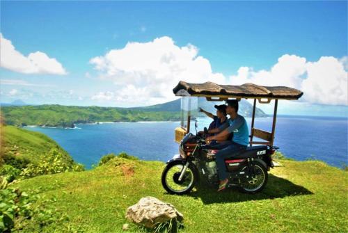 two people riding a motorcycle with a covering on the back at Batanes Seaside Lodge & Restaurant in Basco