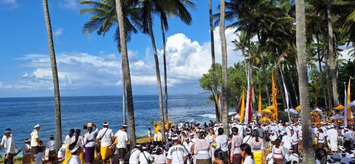 a crowd of people standing on a beach with the ocean at Frangipani Inn & Restaurant in Seraya