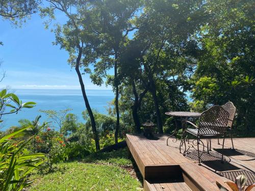 a table and chairs on a wooden deck with a view of the ocean at Gunnadoo Holiday Hut with Ocean Views and Jacuzzi in Miallo