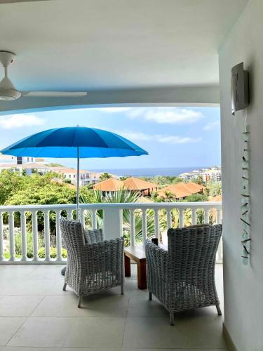 a balcony with chairs and a blue umbrella at Modern appartement bij zee met zwembad op Blue Bay - Tripletree the hill in Sint Michiel