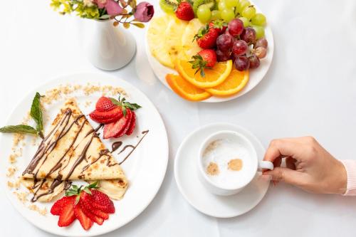 a table with plates of food and a person holding a cup of coffee at Empire Balneo & Spa Hotel in Hisarya