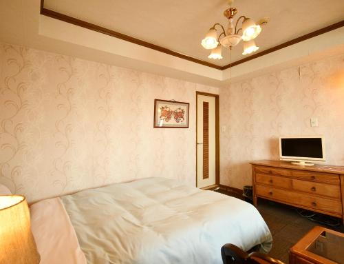 a bedroom with a bed and a desk with a television at Sunrise Hotel Okinawa-どこか懐かしいレトロな雰囲気の宿 in Okinawa City