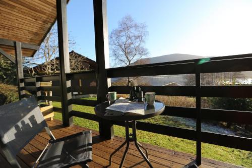 a table and chairs on a deck with a view at Cosy Modern Nordic Lodge w/ Loch View & Log Burner in Lochearnhead