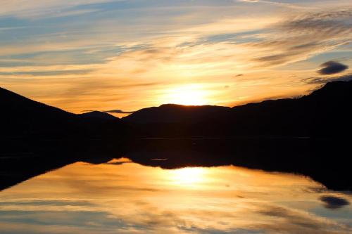 a reflection of a sunset in a lake at Cosy Modern Nordic Lodge w/ Loch View & Log Burner in Lochearnhead