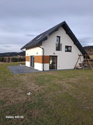 a white house with a black roof on a field at Domek Na Sapisku in Szlembark