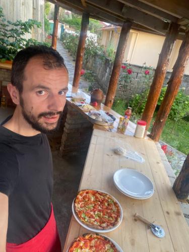 Un hombre sentado en una mesa de madera con dos pizzas. en Meti guest house wooden room, en Krujë