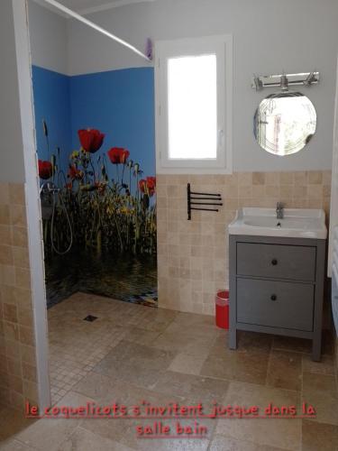 La salle de bains est pourvue d'un lavabo, d'une fenêtre et de fleurs rouges. dans l'établissement Lou mazet, à La Roque-sur-Pernes
