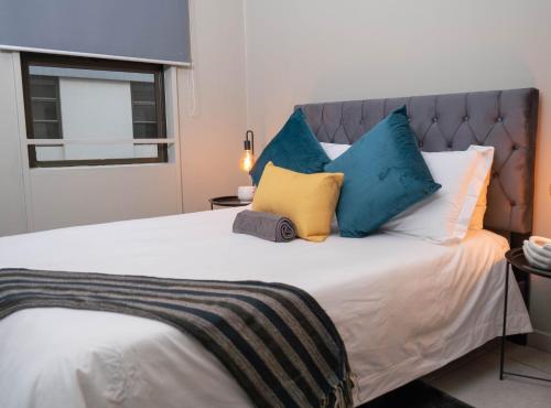 a bed with blue and yellow pillows on it at Two At Urban Pulse in Johannesburg