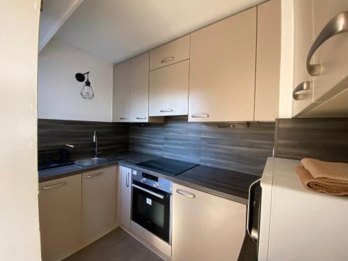 une cuisine avec des armoires blanches, un évier et une cuisinière dans l'établissement Joli 2 pièces parc piscine vue mer, à Vence