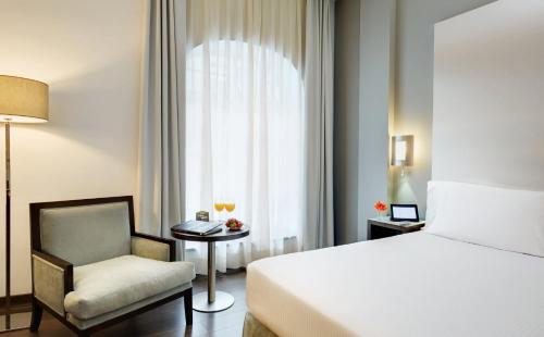 a bedroom with a bed and a chair and a window at Sercotel Coliseo in Bilbao