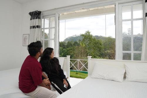 two women sitting on a bed looking out of a window at Mount Edge Riverside Hotel in Bandarawela
