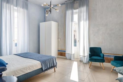 a bedroom with a bed and a chair and windows at Ortigia Amazing Apartment in Siracusa