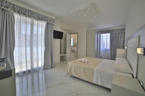 Habitación blanca con cama y ventanas grandes. en Riviera Luxury Rooms, en Porto Cesareo
