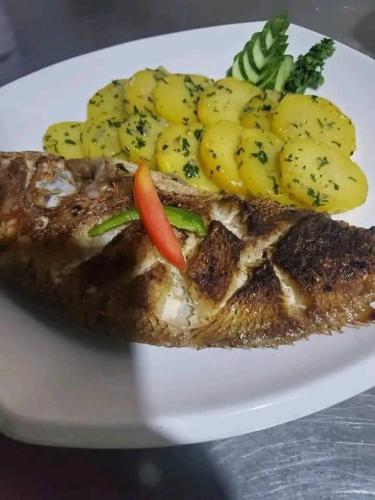 a plate with a piece of fish with potatoes and vegetables at ASVA BEACH Resort in Grand-Popo