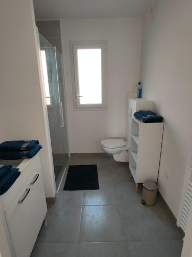 une salle de bain blanche avec toilettes et fenêtre dans l'établissement Appartement à 50 m de la mer, idéal famille, à Langrune-sur-Mer